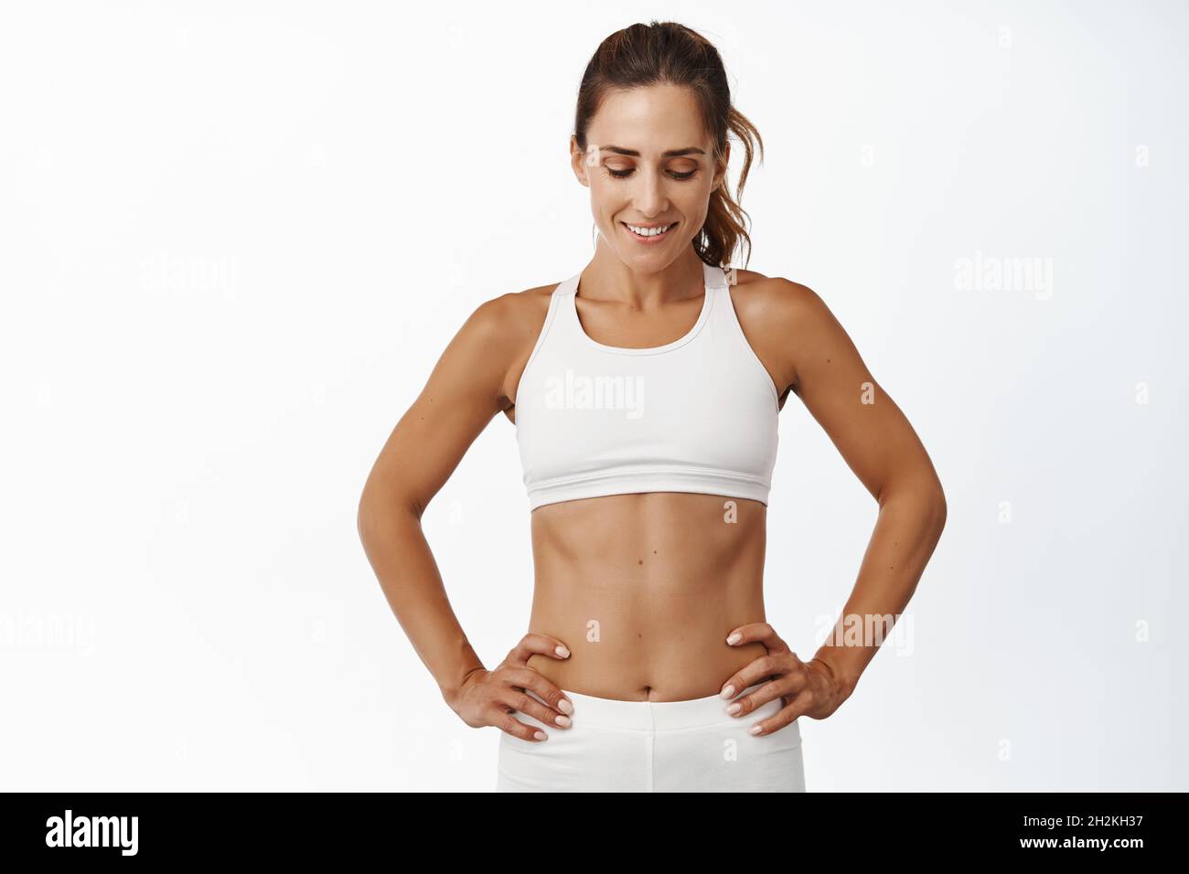 Fitness woman looking down and smiling, taking break, resting after  training in gym, showing her abs, workout against white background Stock  Photo - Alamy