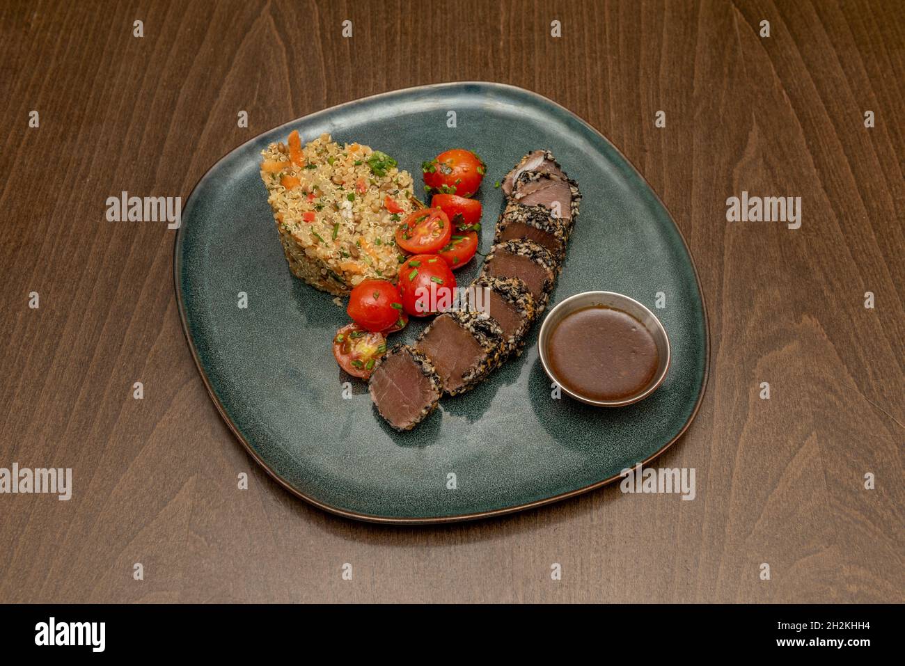 Red tuna tataki recipe accompanied by cherry tomato salad garnished with olive oil and quinoa guranicion with vegetables and sauce on a blue porcelain Stock Photo