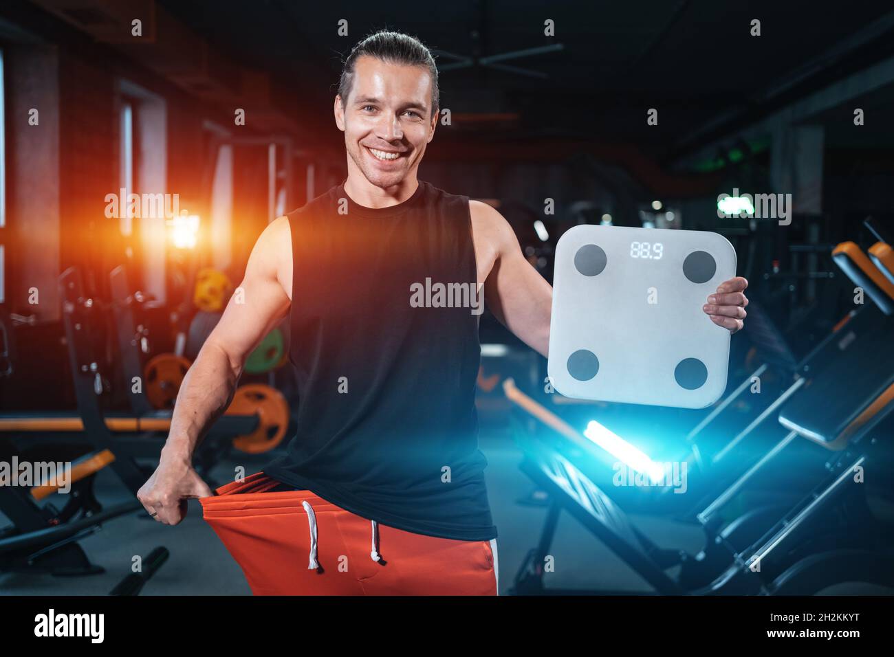 young attractive athlete male weight with scale in gym and dieting Stock Photo