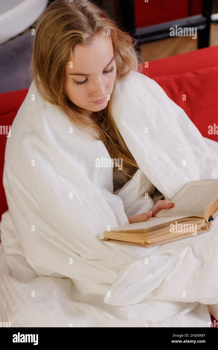 Woman sitting on couch, wrapped in a blanket, reading book Stock Photo