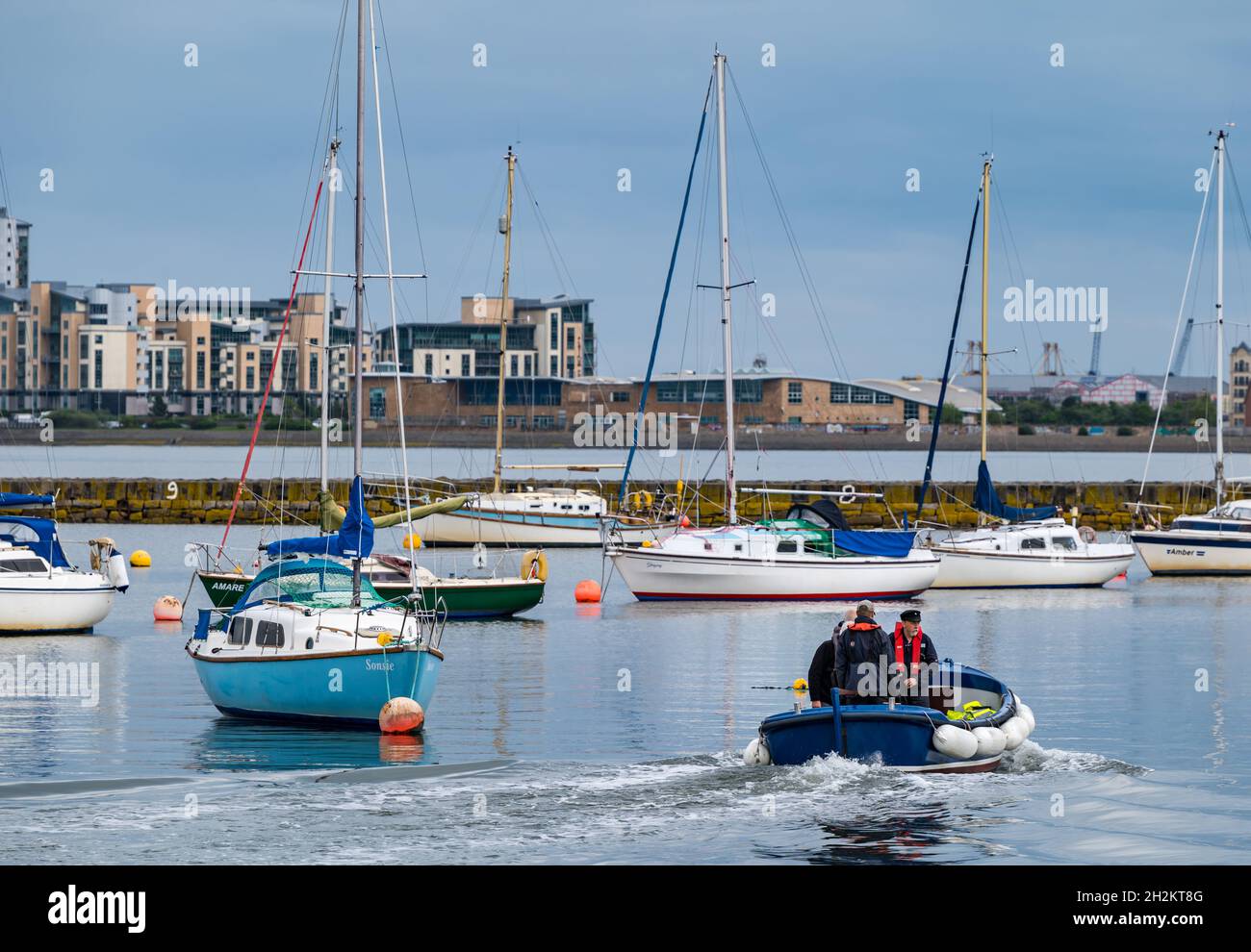 Sailboats in Granton harbour on a sunny day with people in a dinghy, Edinburgh, Scotland, UK Stock Photo