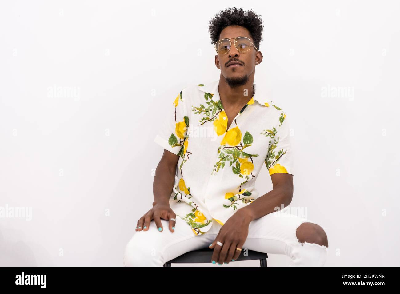 Young Cuban man in floral shirt and sunglasses sitting and posing on a white background Stock Photo