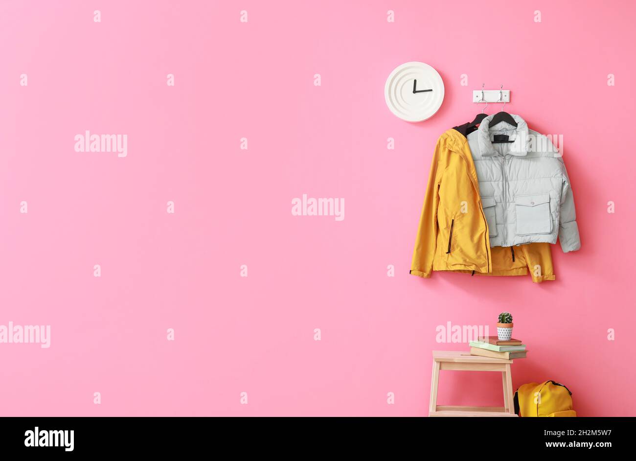 Stylish jackets and clock hanging on pink wall in hallway Stock Photo