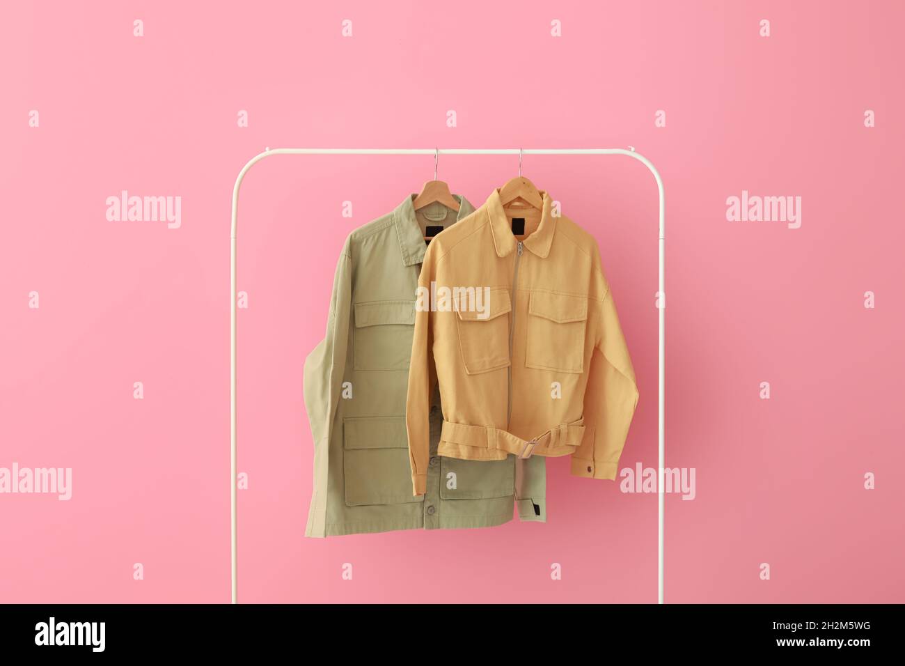 Rack with green and yellow jackets near pink wall Stock Photo