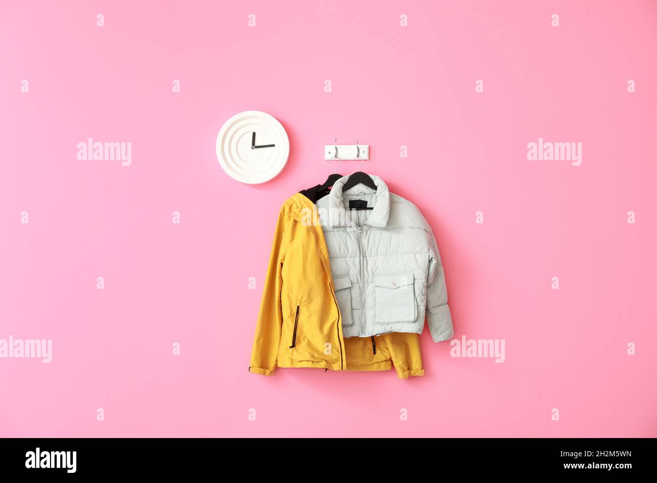 Stylish jackets and clock hanging on pink wall Stock Photo