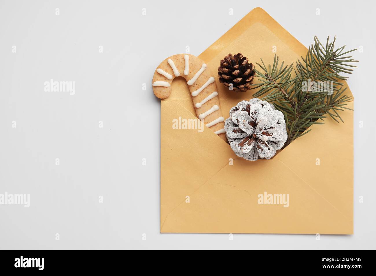 Envelope with fir tree branch, cookie and pine cones on white ...