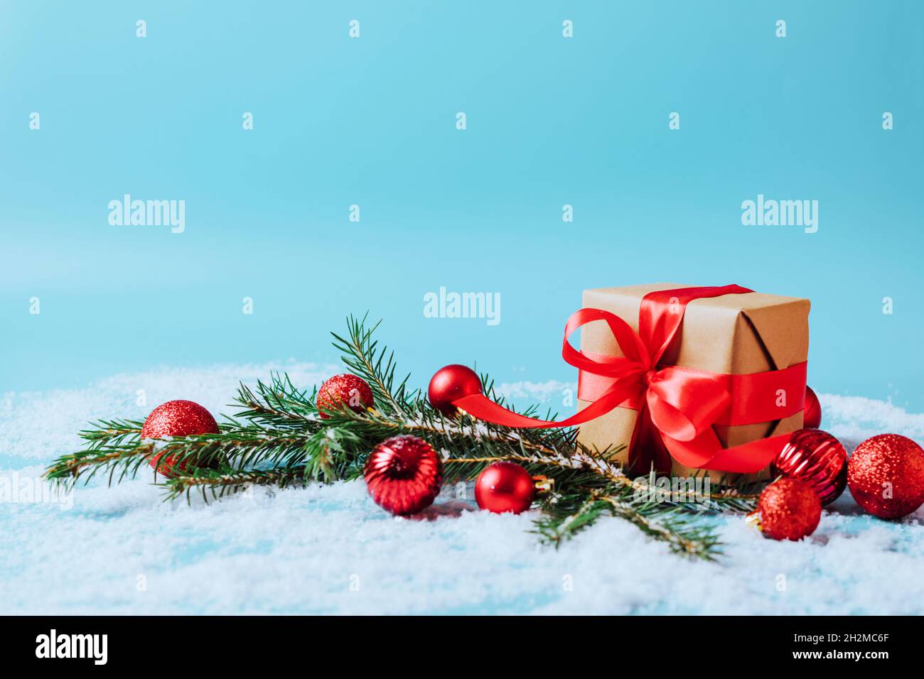 Festive box with a red bow on a blue background with Christmas toys balls branch of fluffy spruce sparkles and confetti . New Year Christmas concept Stock Photo