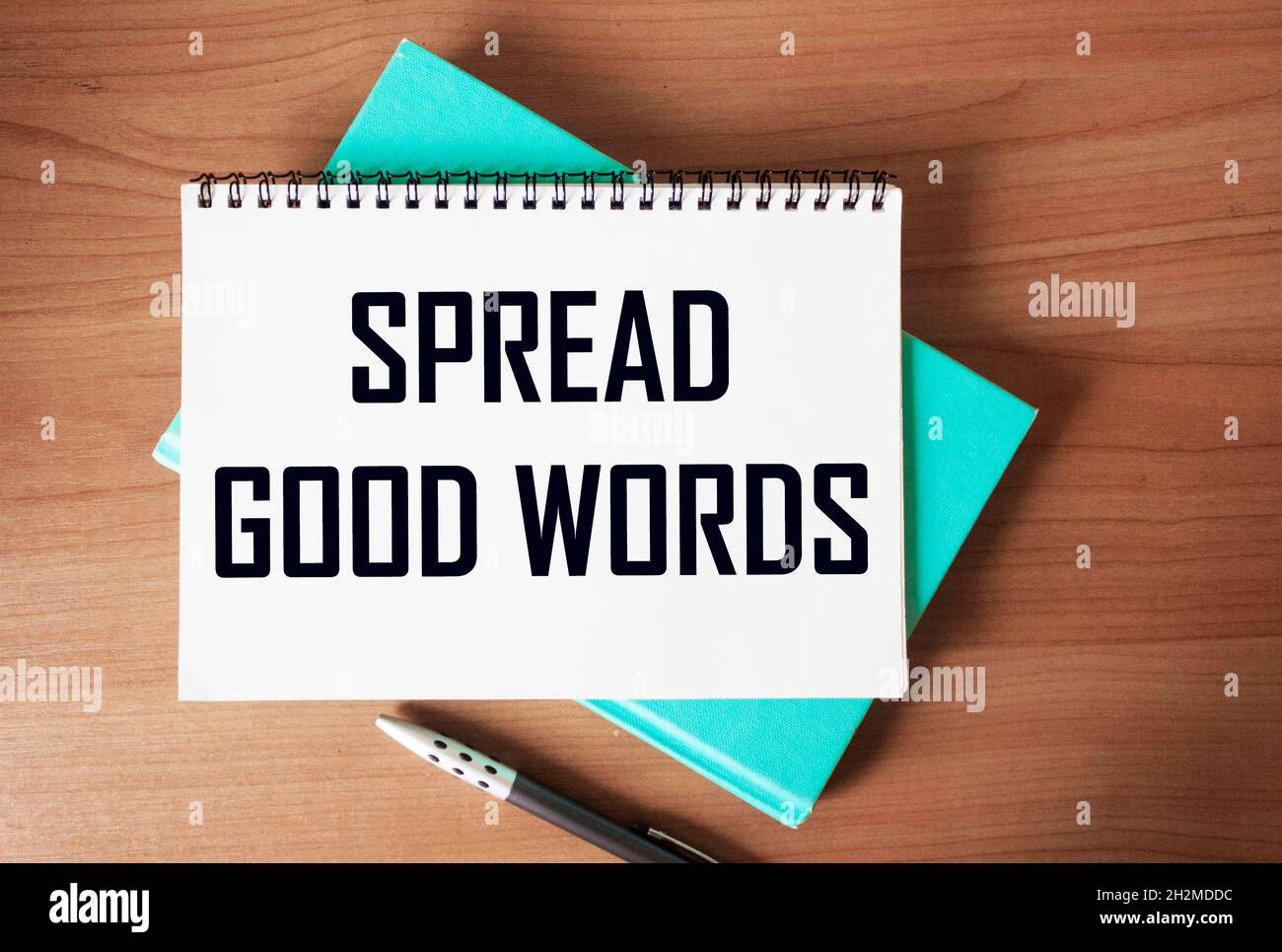 the text SPREAD GOOD WORDS is written on a notebook and on a wooden table . Stock Photo