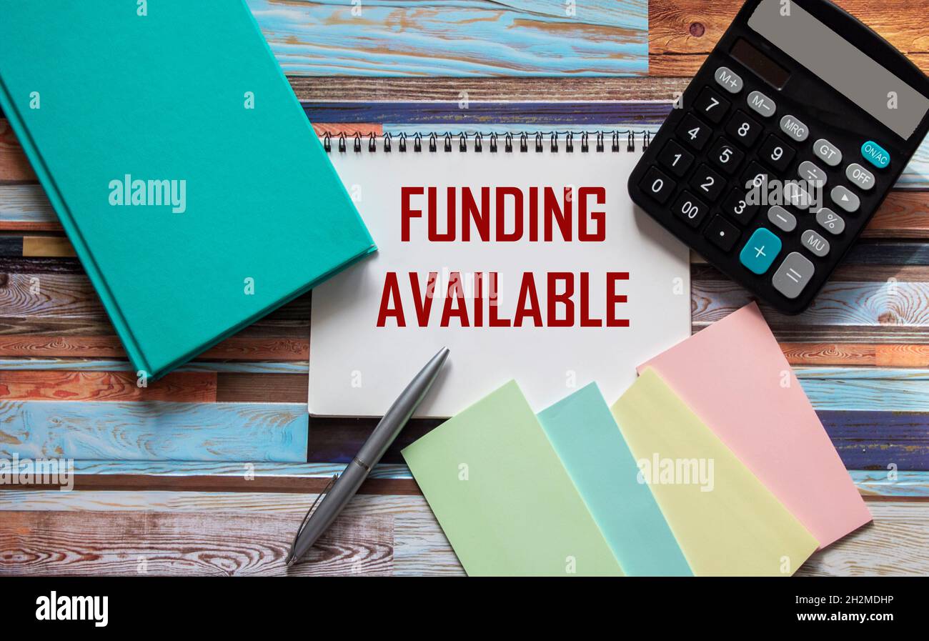 Funding Available text on notepad, next to calculator, sticker, pen and green notepad. Sponsored funding business start-up projects concept. Stock Photo