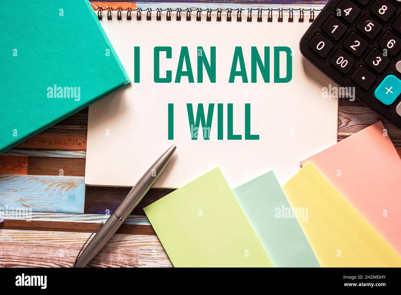 I can and I will be written on a notebook, next to colored stickers, a diary, a calculator and a pen. Striped background Stock Photo