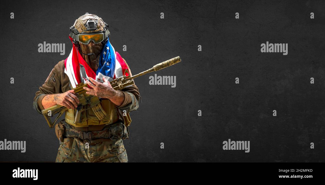 An American infantry soldier stands against the background of a concrete wall with a flag on his shoulders. Concept of the day of remembrance of veter Stock Photo