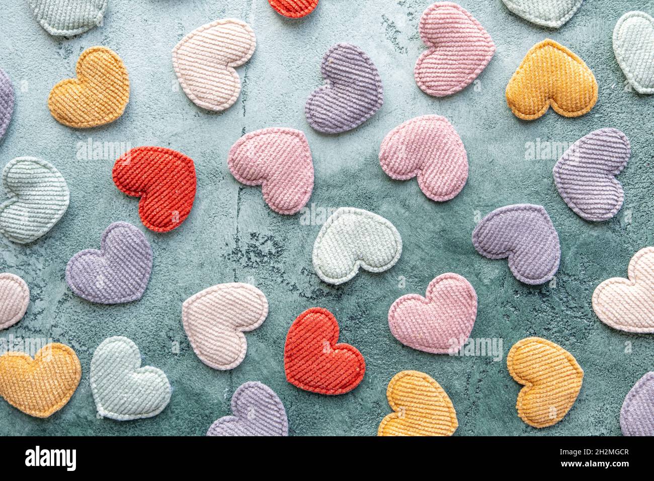 A scattering of multicolored velvet hearts on a green textured background. Flat lay. Valentine's Day. The concept of decor, needlework. Stock Photo