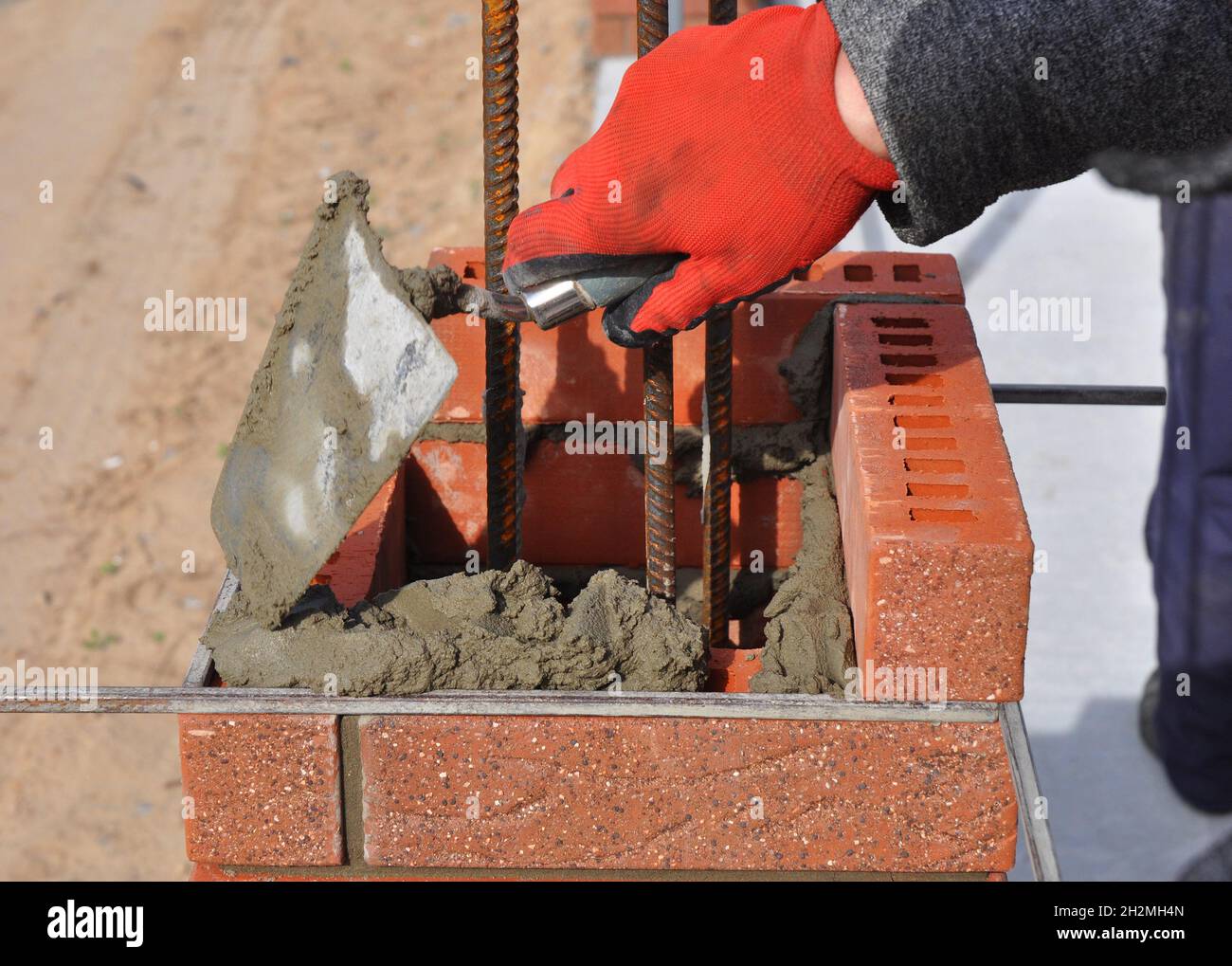 Bricklayer worker installing red blocks and caulking brick masonry