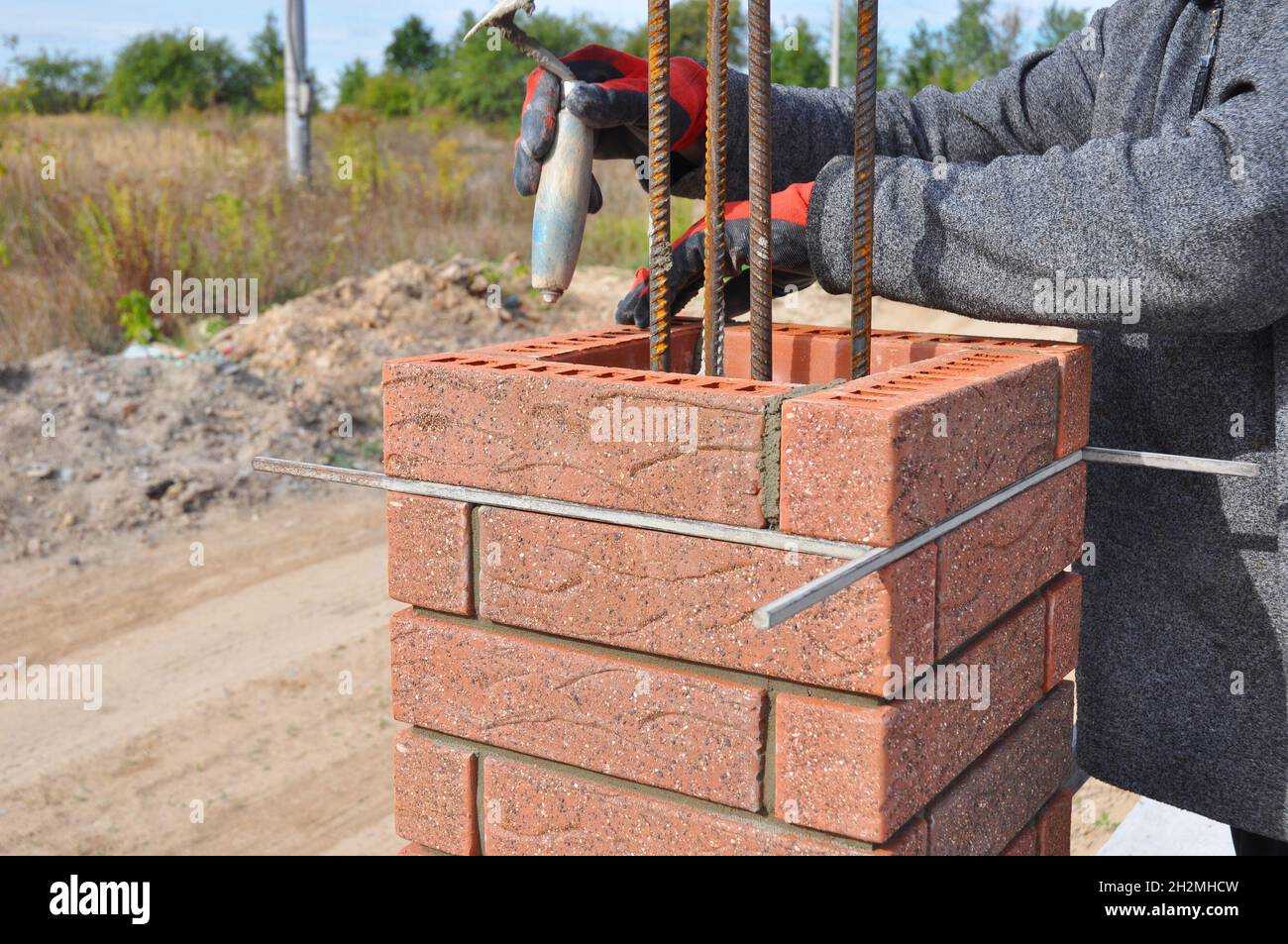 Bricklayer Worker Installing Red Clinker Blocks around Iron Bar and