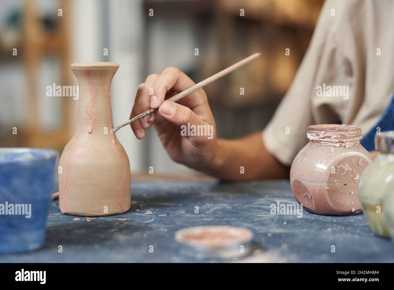 Close-up of unrecognizable potter using paintbrush while applying pink paint on clay vase in workshop Stock Photo