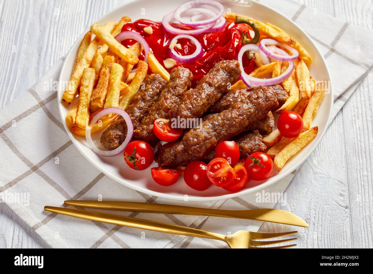 close-up of cevapcici, grilled balkan sausages with potato fries, red onion  rings, red pepper, tomatoes on a white plate on a wooden table Stock Photo  - Alamy
