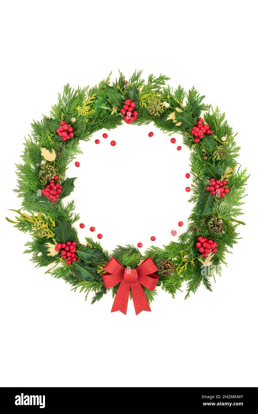 Abstract Christmas wreath with red bow, holly, loose berries, ivy, mistletoe and cedar leaves on white background. Composition for winter solstice, Xm Stock Photo