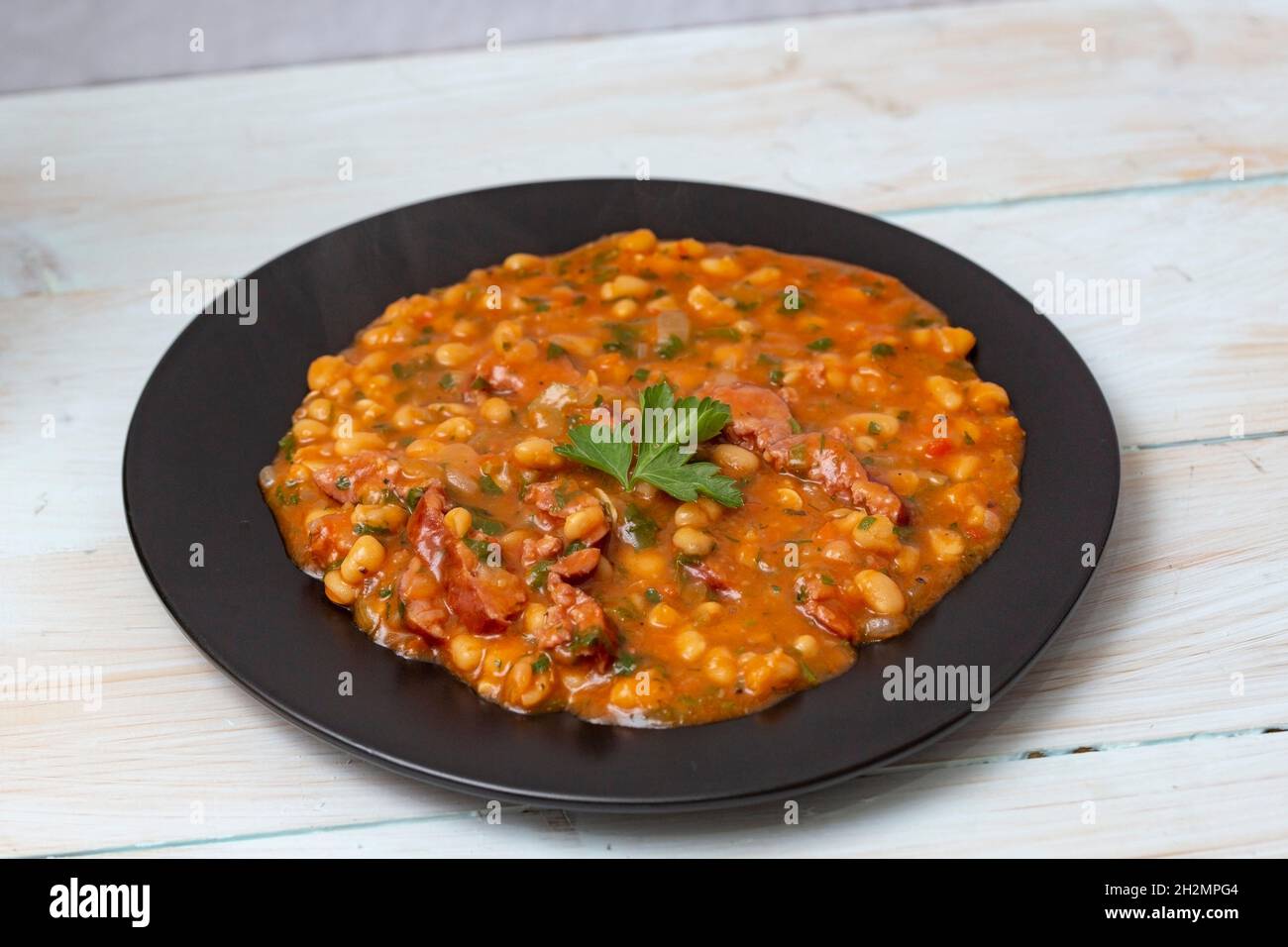 Beans with sausages on a black ceramic plate Stock Photo