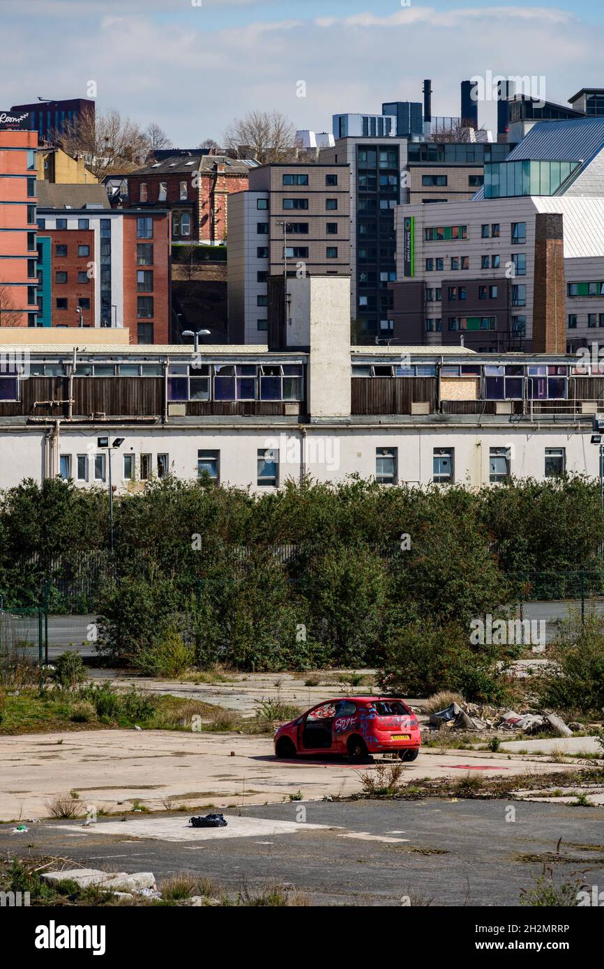 Developed land (student apartments development) & derelict waste ground (abandoned vandalised vehicle, brownfield site) - Leeds, Yorkshire, England UK Stock Photo