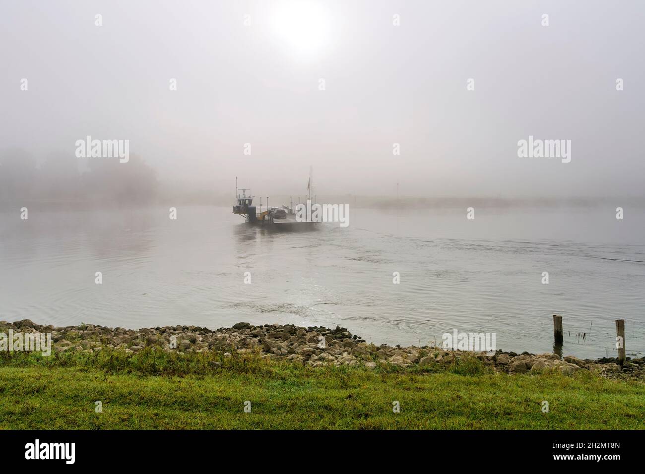 Ferry crossing river IJssel on a misty autumn morning at sunrise. Stock Photo