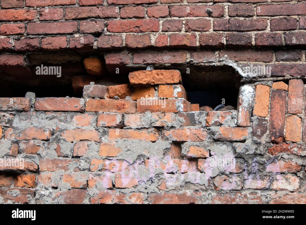 Old half destroyed stone wall of red bricks with big pothole Stock Photo