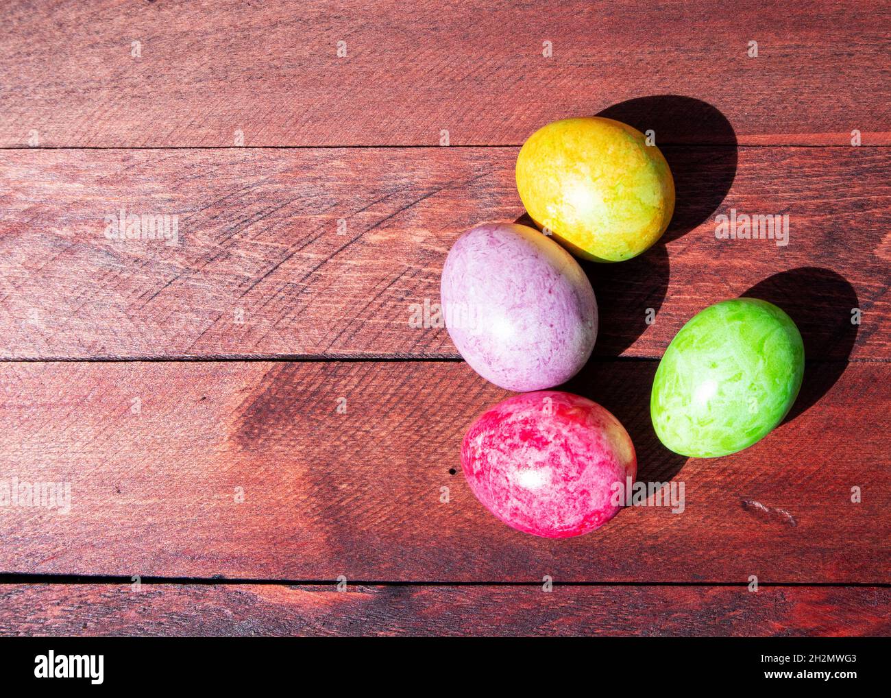 Four multicolored bright easter eggs lying on sunlit red wood deck Stock Photo