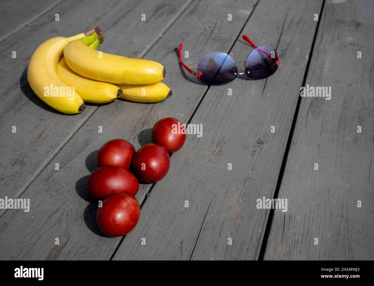 Mix composition with painted easter eggs, bunch of ripe bananas and sunglasses lying on an old wooden surface Stock Photo