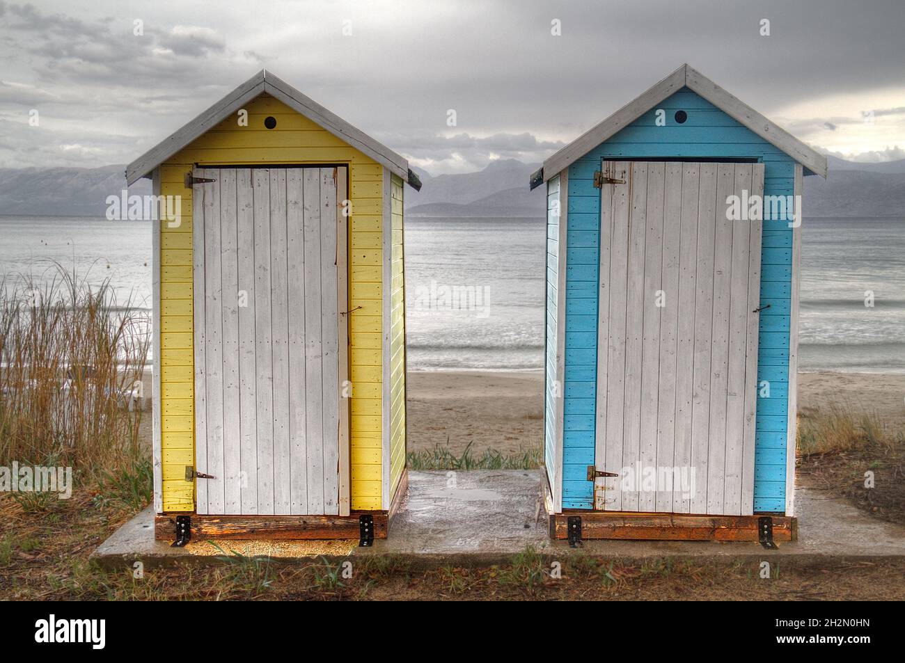 Two small blue and yellow portable toilet houses on the beach on a dark, drizzly day Stock Photo