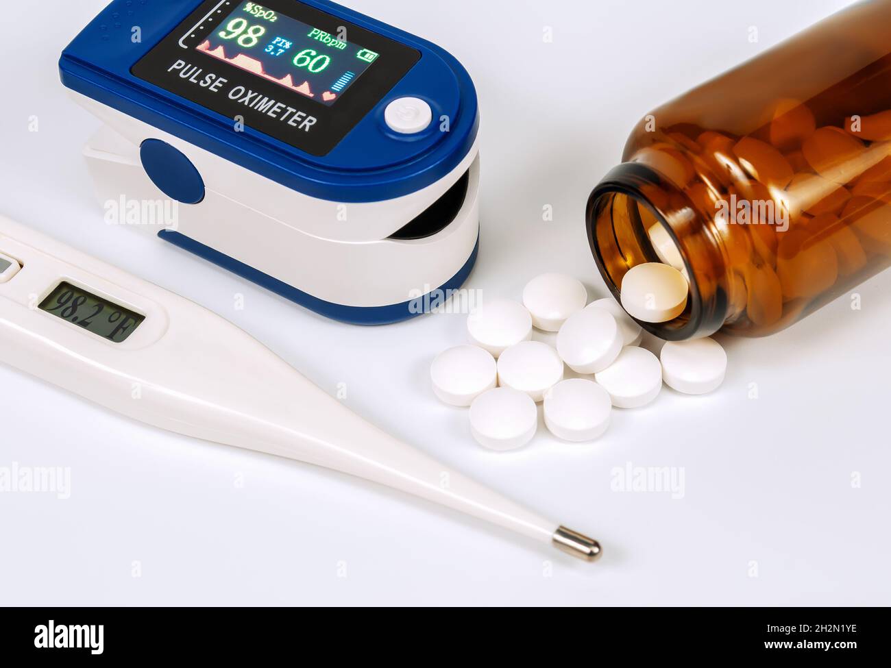 brown glass bottle with white pills, thermometer and pulse oximeter on white background Stock Photo