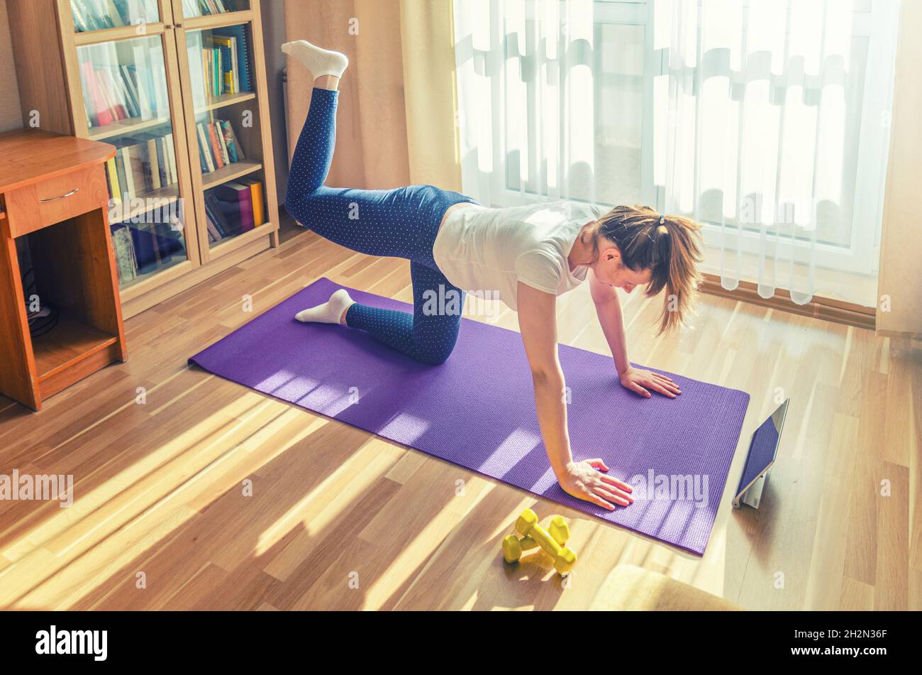 Young woman doing workout sports at home, straight-leg donkey kick on ...