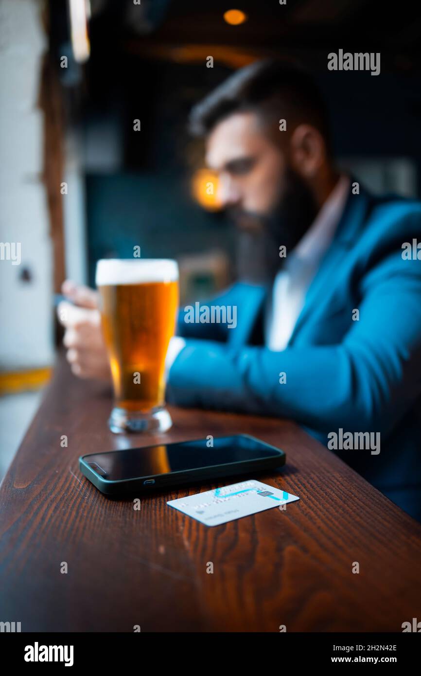 A businessman in a bar using his smartphone and a credit card Stock Photo