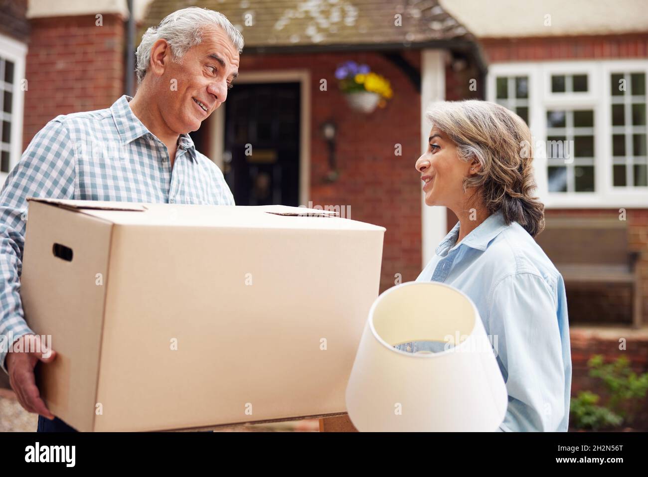 Portrait Of Mature Couple Carrying Boxes On Moving Day In Front Of Dream Home Stock Photo