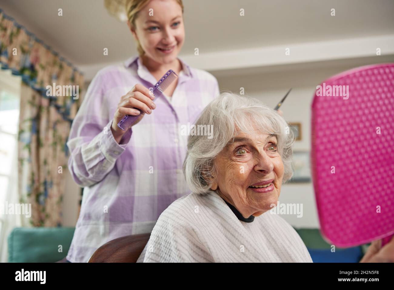 Female Mobile Hairdresser Cutting Senior Womans Hair At Home Stock