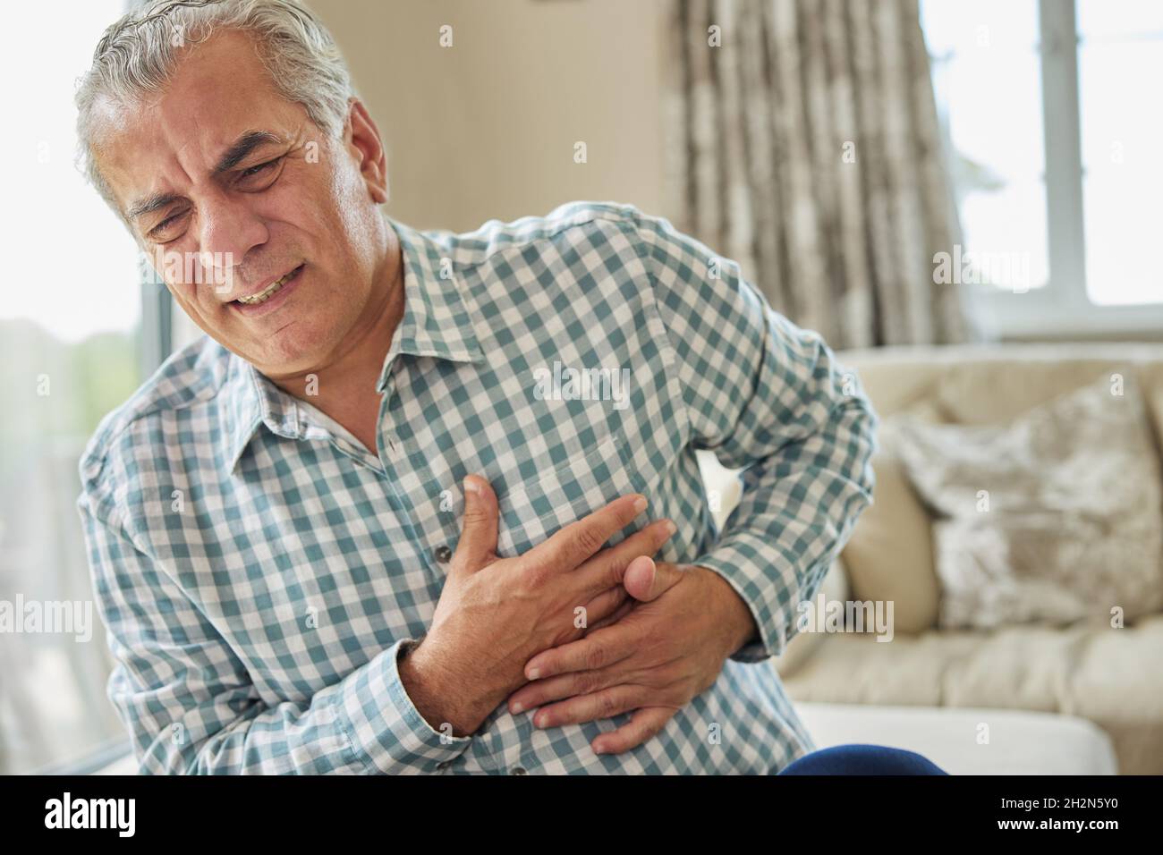 Mature Man Clutching Chest And Suffering Heart Attack At Home Stock Photo