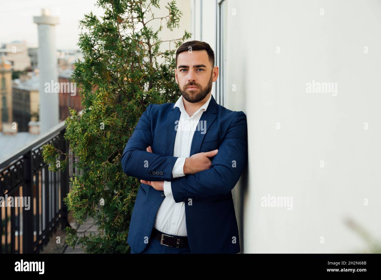 Serious businessman with arms crossed leaning on wall in office balcony ...