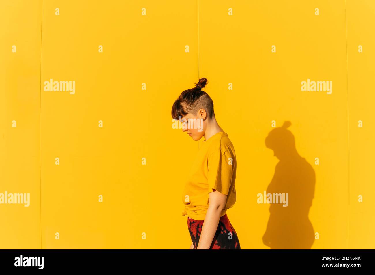 Androgynous person with half-shaved hairstyle standing by yellow wall Stock Photo