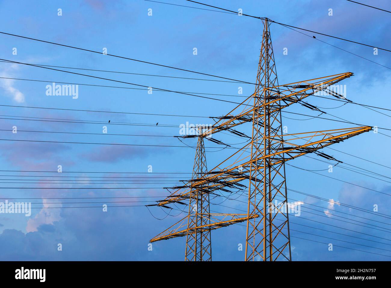 Electricity pylons standing against blue cloudy sky Stock Photo - Alamy