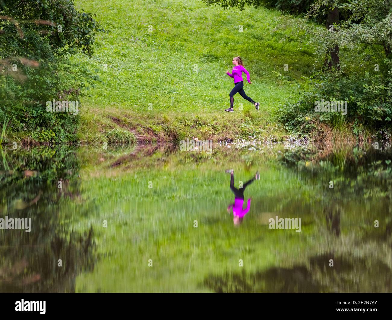 Female athlete running by lake in forest Stock Photo