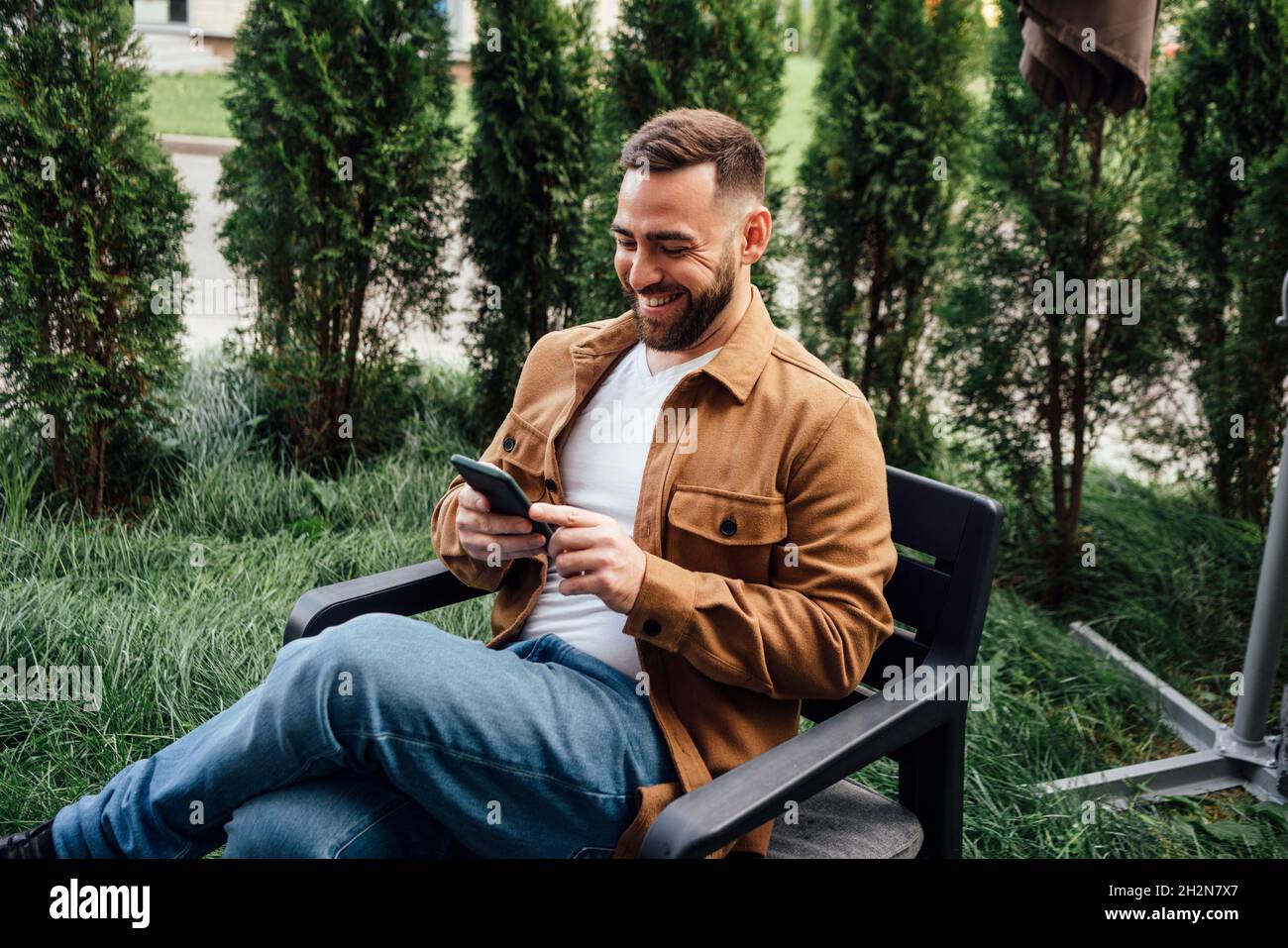 Smiling businessman text messaging through mobile phone at backyard Stock Photo