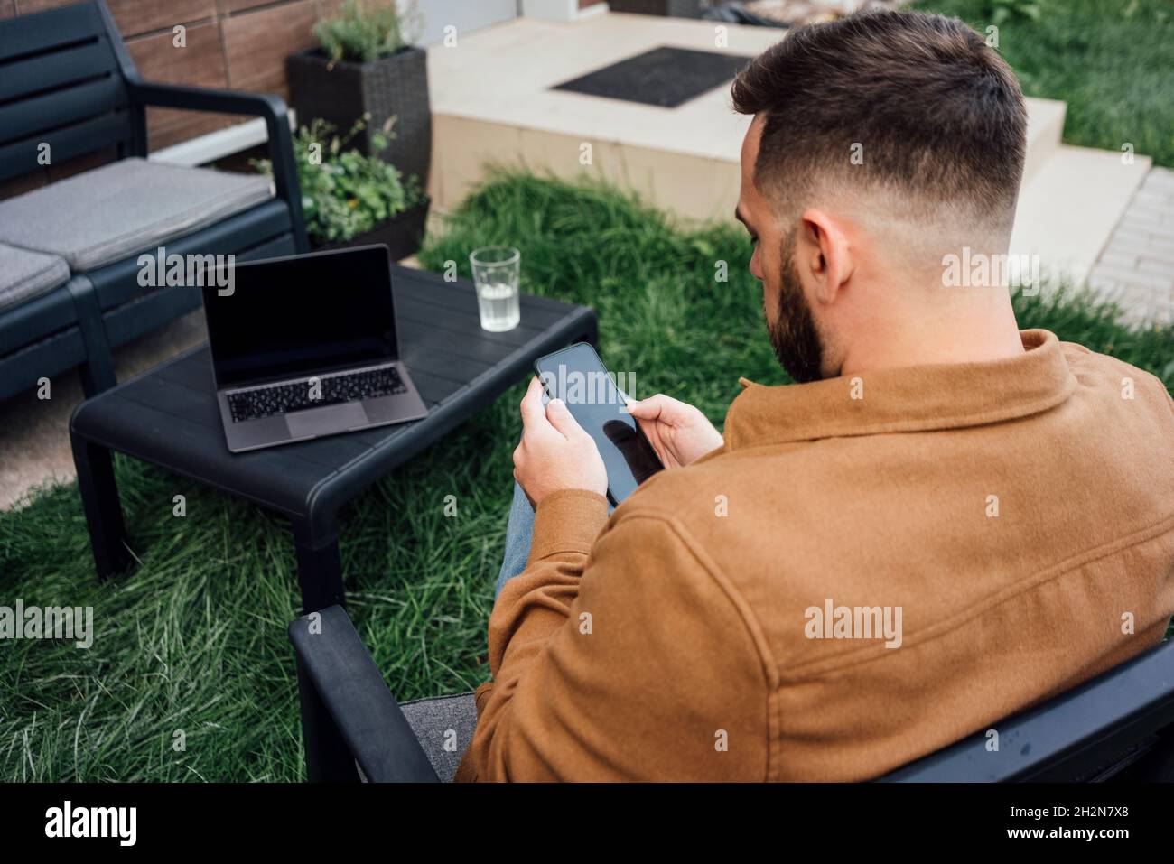 Male freelancer text messaging through smart phone while sitting at backyard Stock Photo