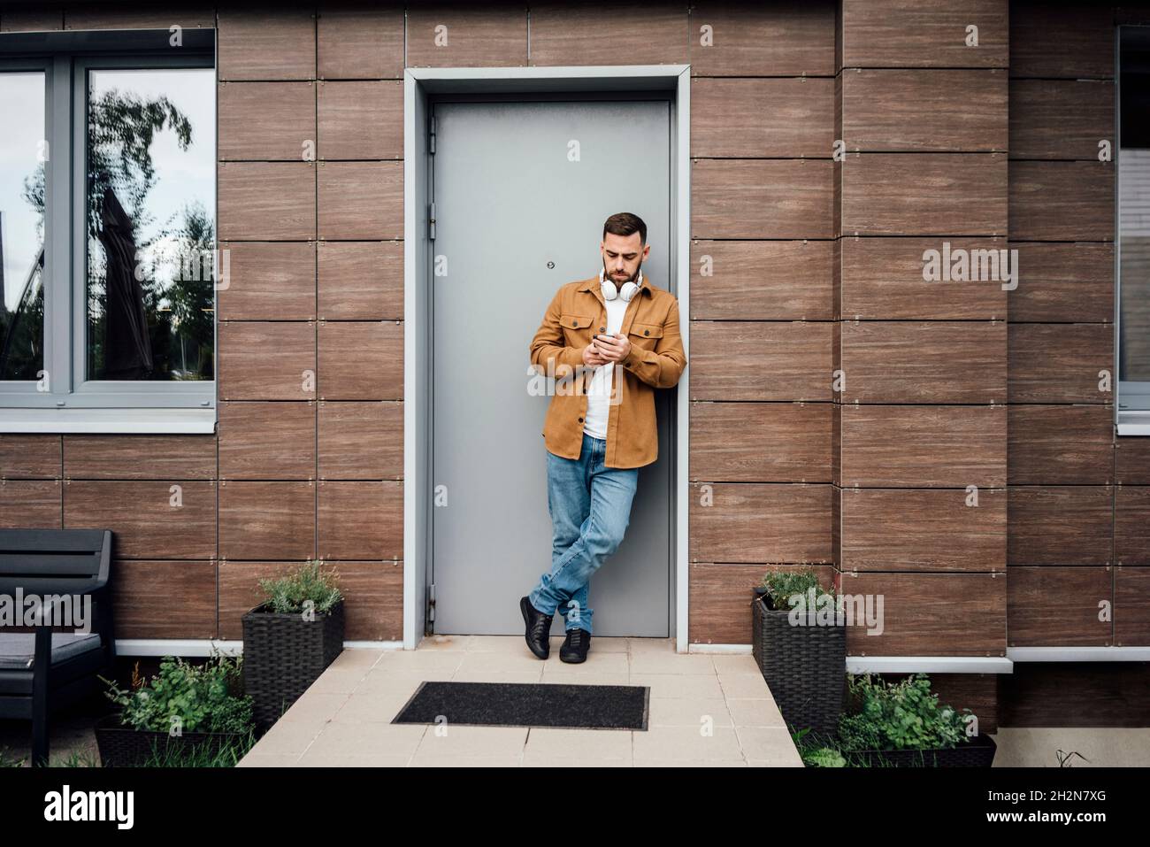 Man using mobile phone while leaning at doorway Stock Photo