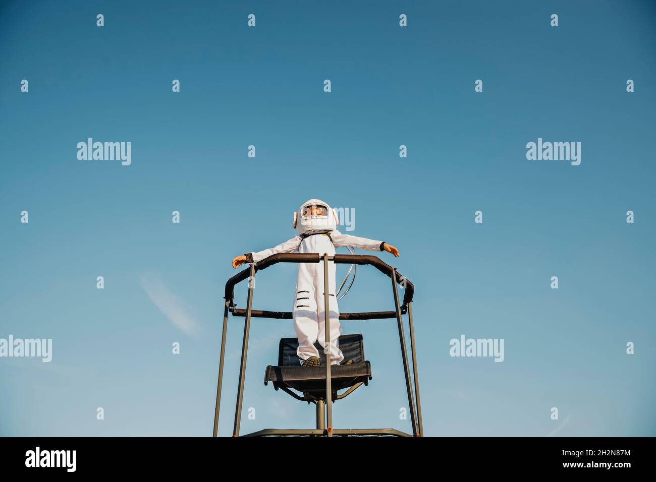 Boy wearing space suit standing with arms outstretched on chair Stock Photo