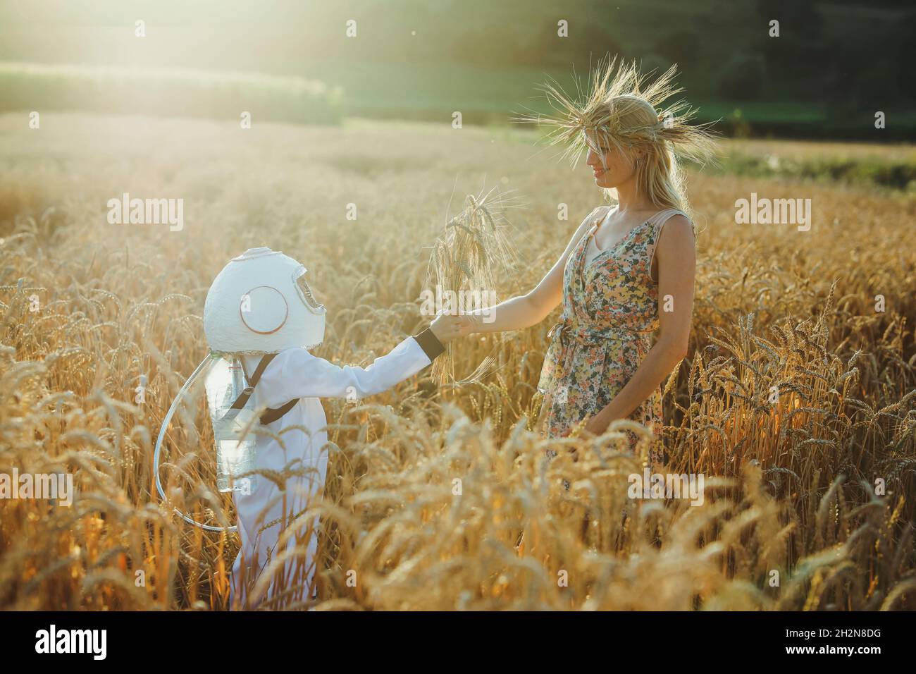 Male astronaut boy giving wheat crops to mother at field Stock Photo