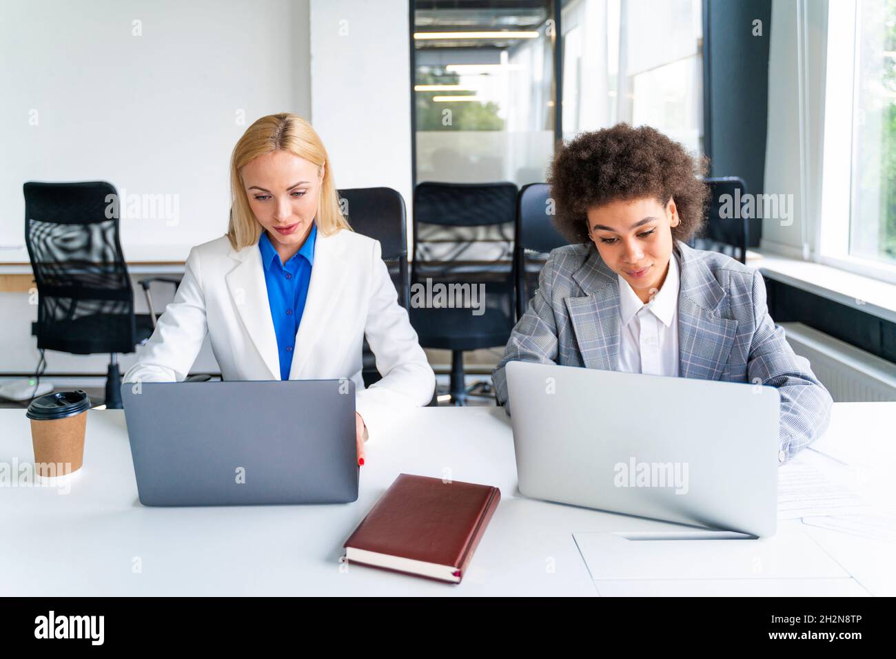 Female coworkers using laptops while working in office Stock Photo