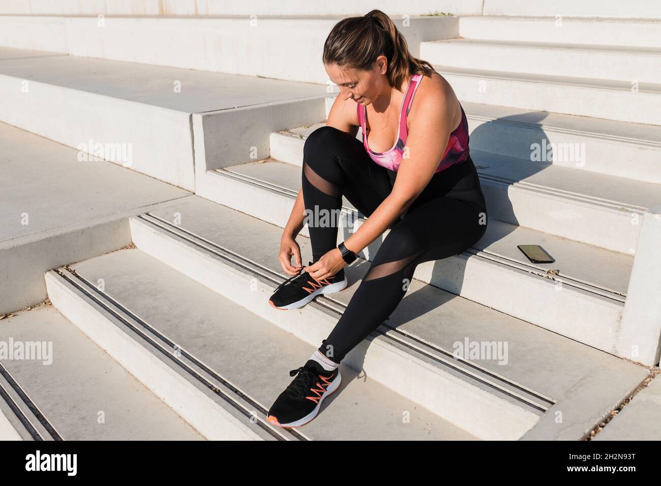 Female athlete tying shoelace while sitting on steps Stock Photo