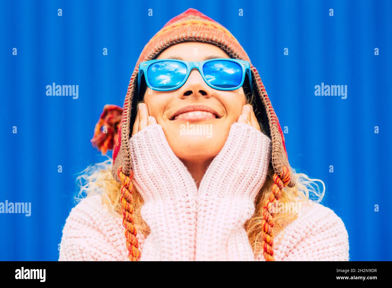Smiling woman wearing sunglasses and knit hat while touching face Stock Photo