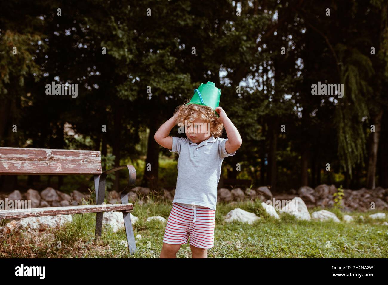 cute-blond-boy-wearing-bucket-on-head-standing-by-bench-at-backyard