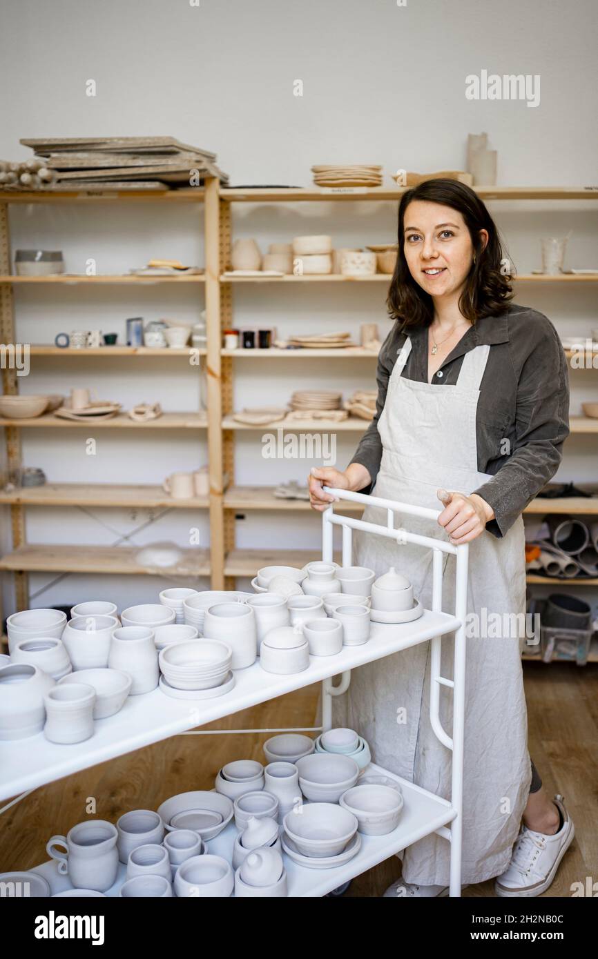 Smiling young craftswoman with pottery cart in workshop Stock Photo - Alamy