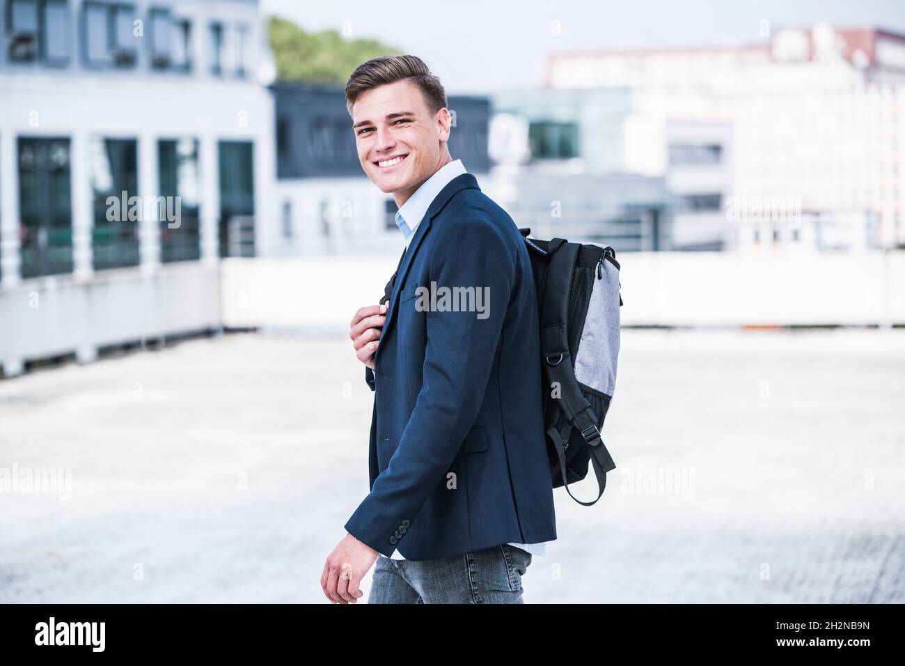 Smiling businessman with backpack walking on rooftop Stock Photo