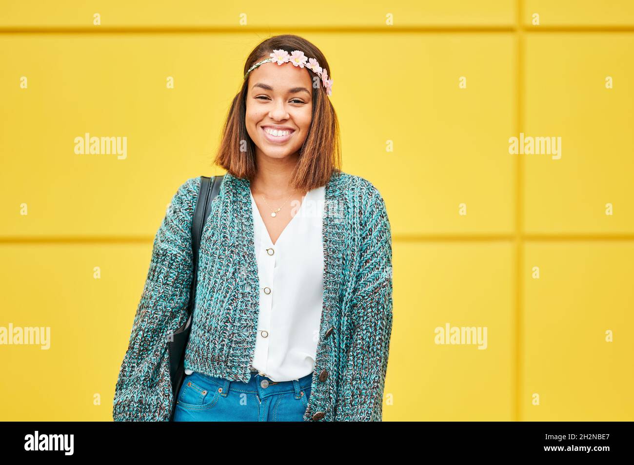Smiling woman wearing flower tiara standing in front of yellow wall Stock Photo
